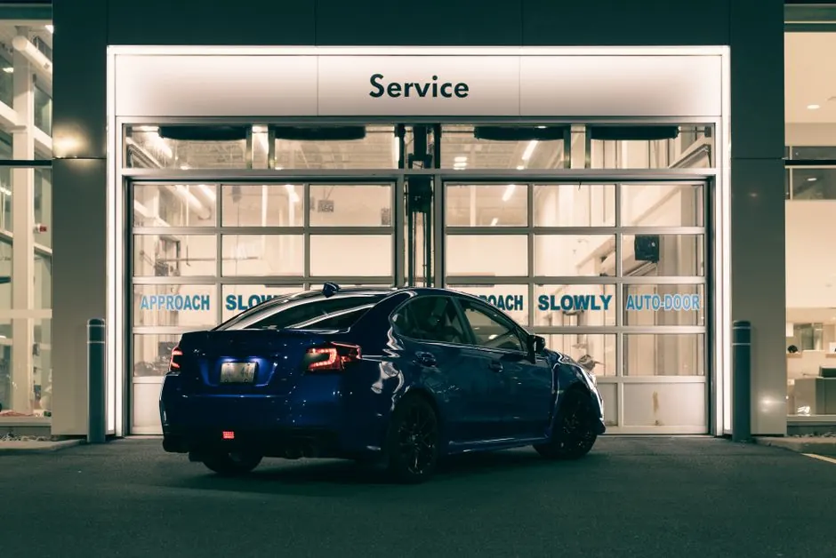 A sleek blue car parked at a service station entrance illuminated at night with modern lighting.