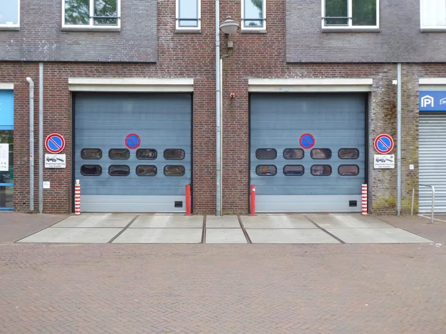 Closed industrial garage doors with no parking signs and brick facade.