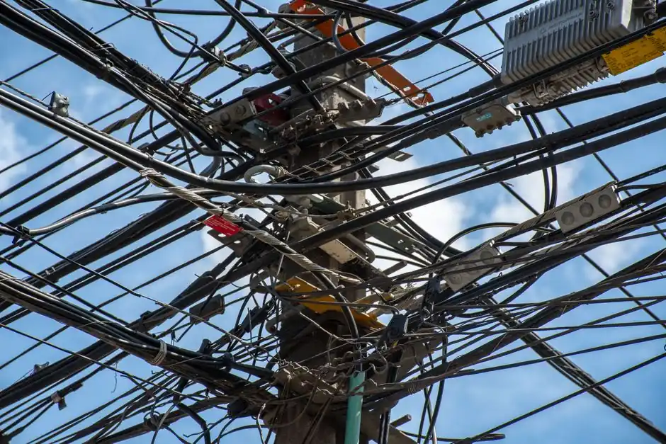 Tangled power lines and cables interwoven on a utility pole in Santiago, Chile against a clear sky.