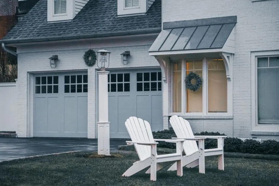 Two white Adirondack chairs in front of a cozy suburban home.